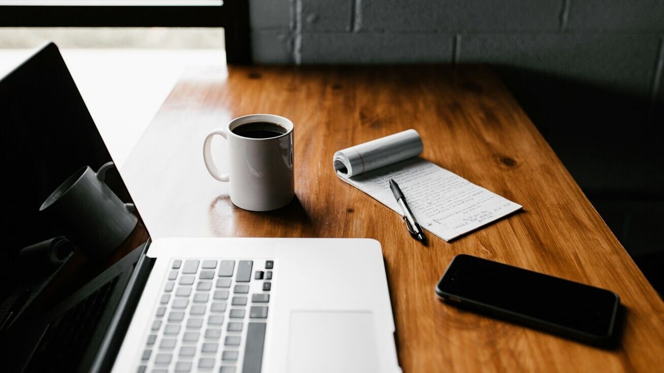 Schreibtisch mit Laptop, Notizbuch, Stift und einer Tasse Kaffee für produktives Arbeiten