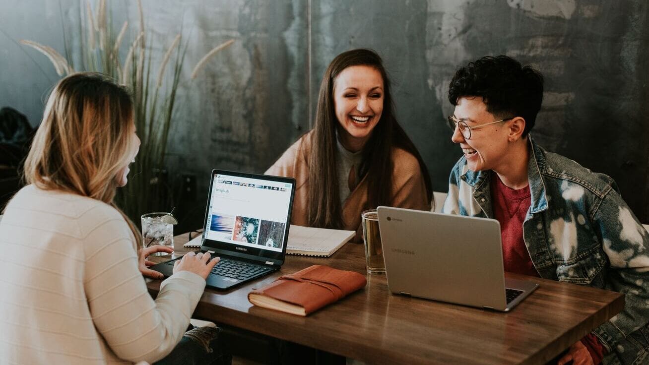 Drei Kollegen lächeln und arbeiten zusammen an Laptops, was Zusammenarbeit und Lernen mit der HubSpot Academy darstellt